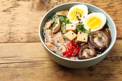 Bowl of delicious ramen on wooden table, space for text. Noodle soup