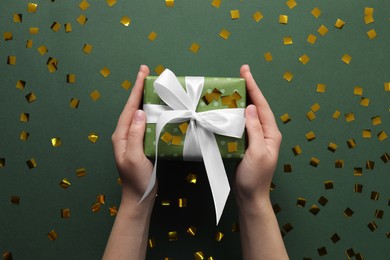 Woman with Christmas gift and confetti on green background, top view