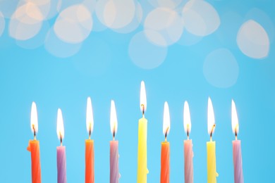 Photo of Hanukkah celebration. Burning candles on light blue background with blurred lights, space for text