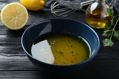 Photo of Bowl with lemon sauce on black wooden table. Delicious salad dressing