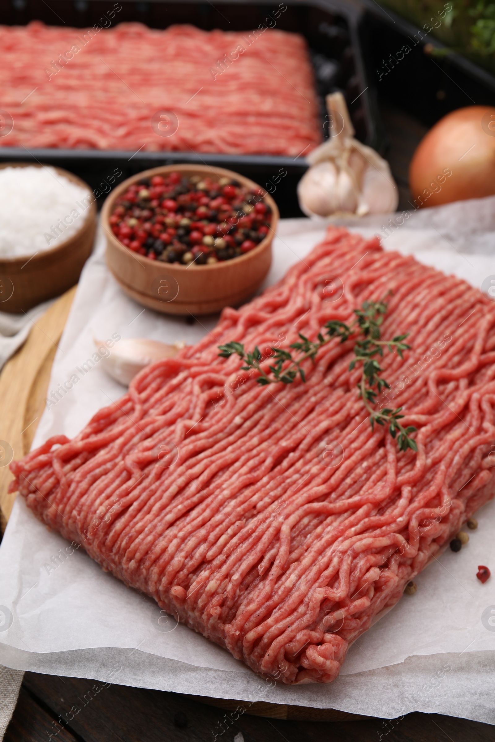 Photo of Fresh raw ground meat, thyme and peppercorns on table, closeup