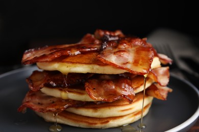 Delicious pancakes with maple syrup and fried bacon on plate, closeup