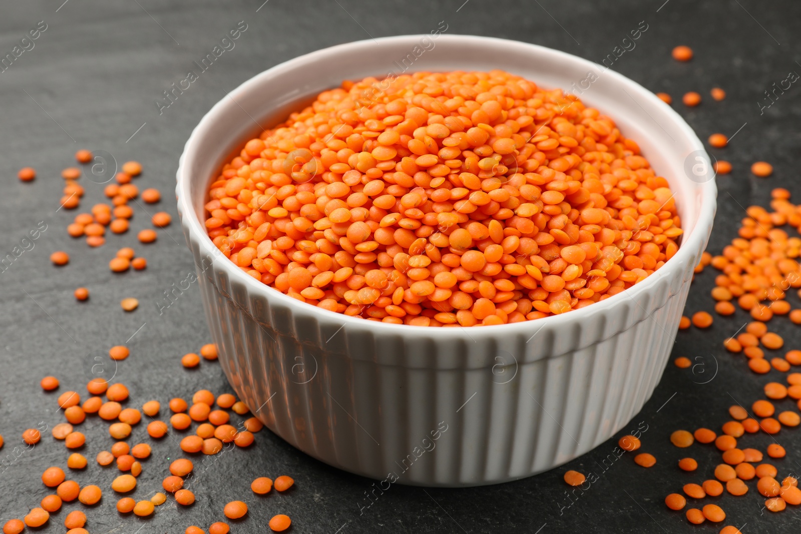 Photo of Raw red lentils in bowl on grey table, closeup