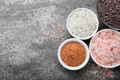 Different kinds of salt on grey table, flat lay. Space for text