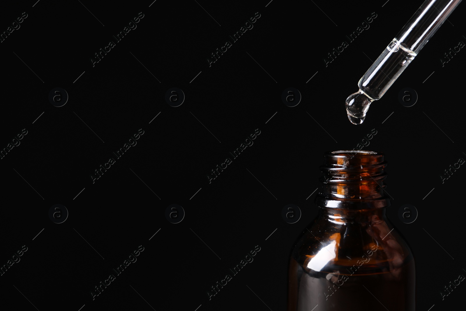 Photo of Dripping cosmetic serum from pipette into bottle on black background, closeup and space for text