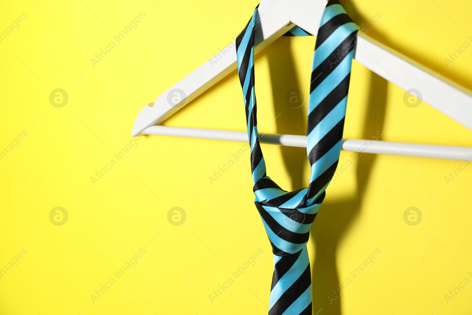 Photo of Hanger with striped necktie on yellow background, closeup. Space for text