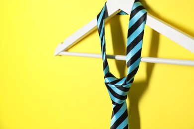 Hanger with striped necktie on yellow background, closeup. Space for text