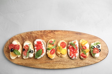 Wooden board with delicious tomato bruschettas on light grey background, top view