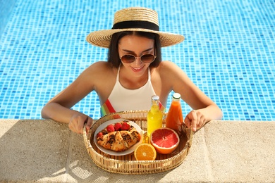 Young woman with delicious breakfast on tray in swimming pool