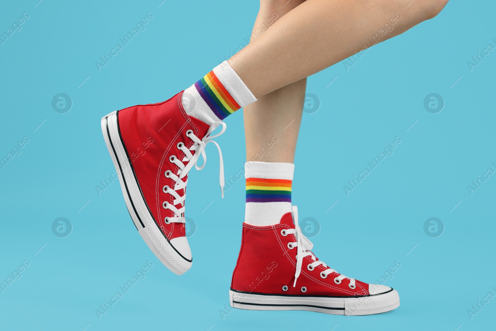 Photo of Woman in stylish gumshoes on light blue background, closeup