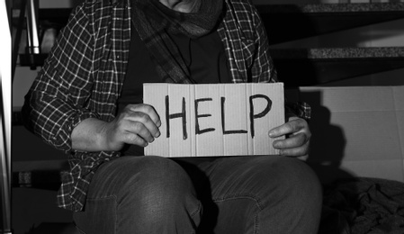 Photo of Poor senior man with cardboard sign HELP on stairs indoors. Black and white effect