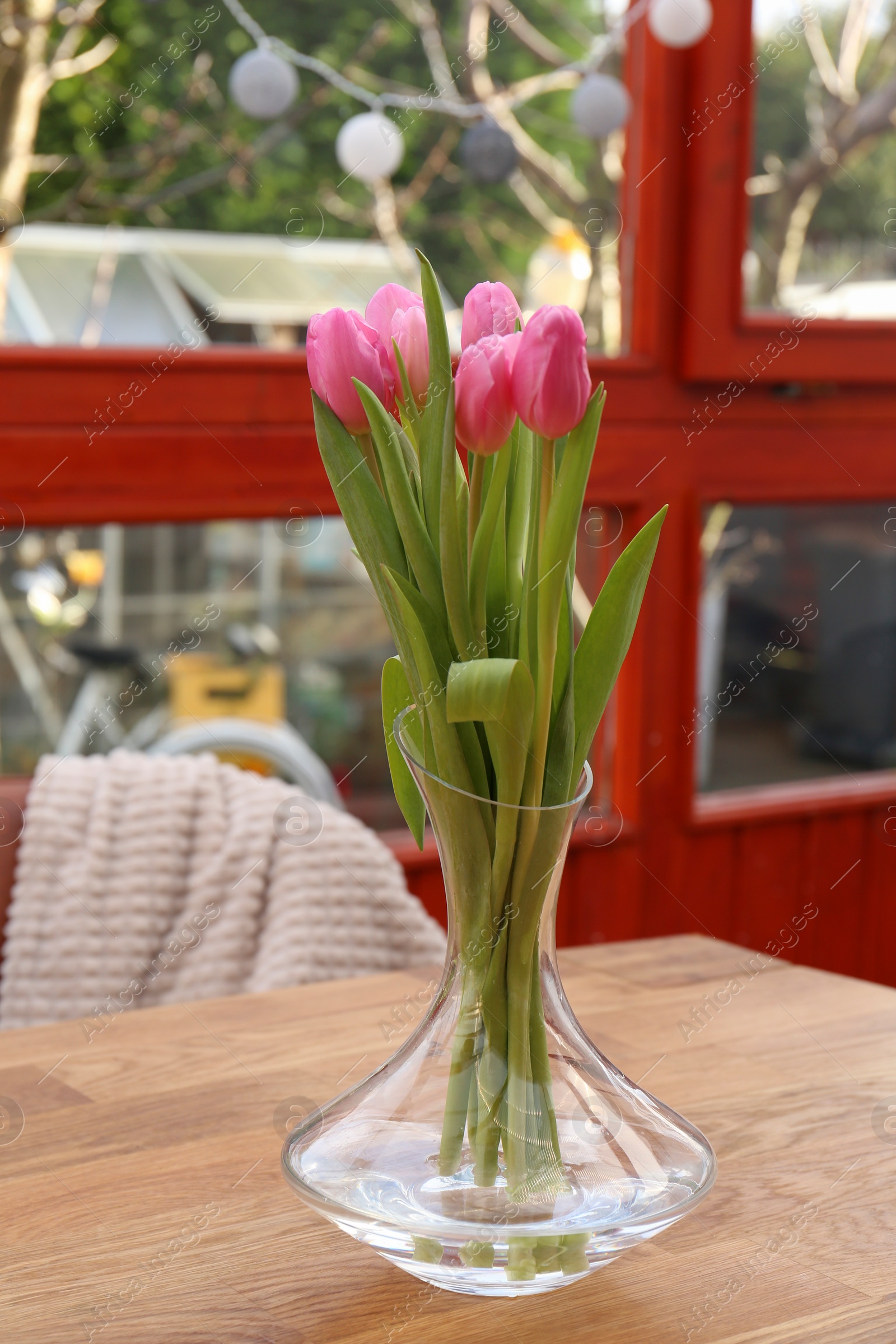 Photo of Pink tulips in glass vase on wooden table at terrace