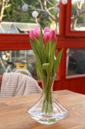 Pink tulips in glass vase on wooden table at terrace