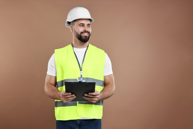 Engineer in hard hat holding clipboard on brown background