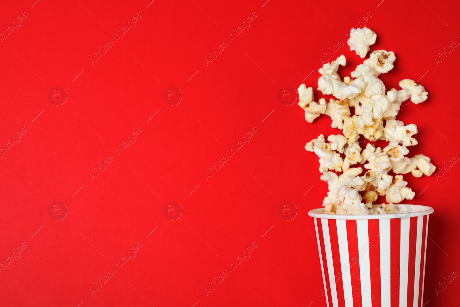 Photo of Overturned paper cup with tasty popcorn on color background, top view. Space for text