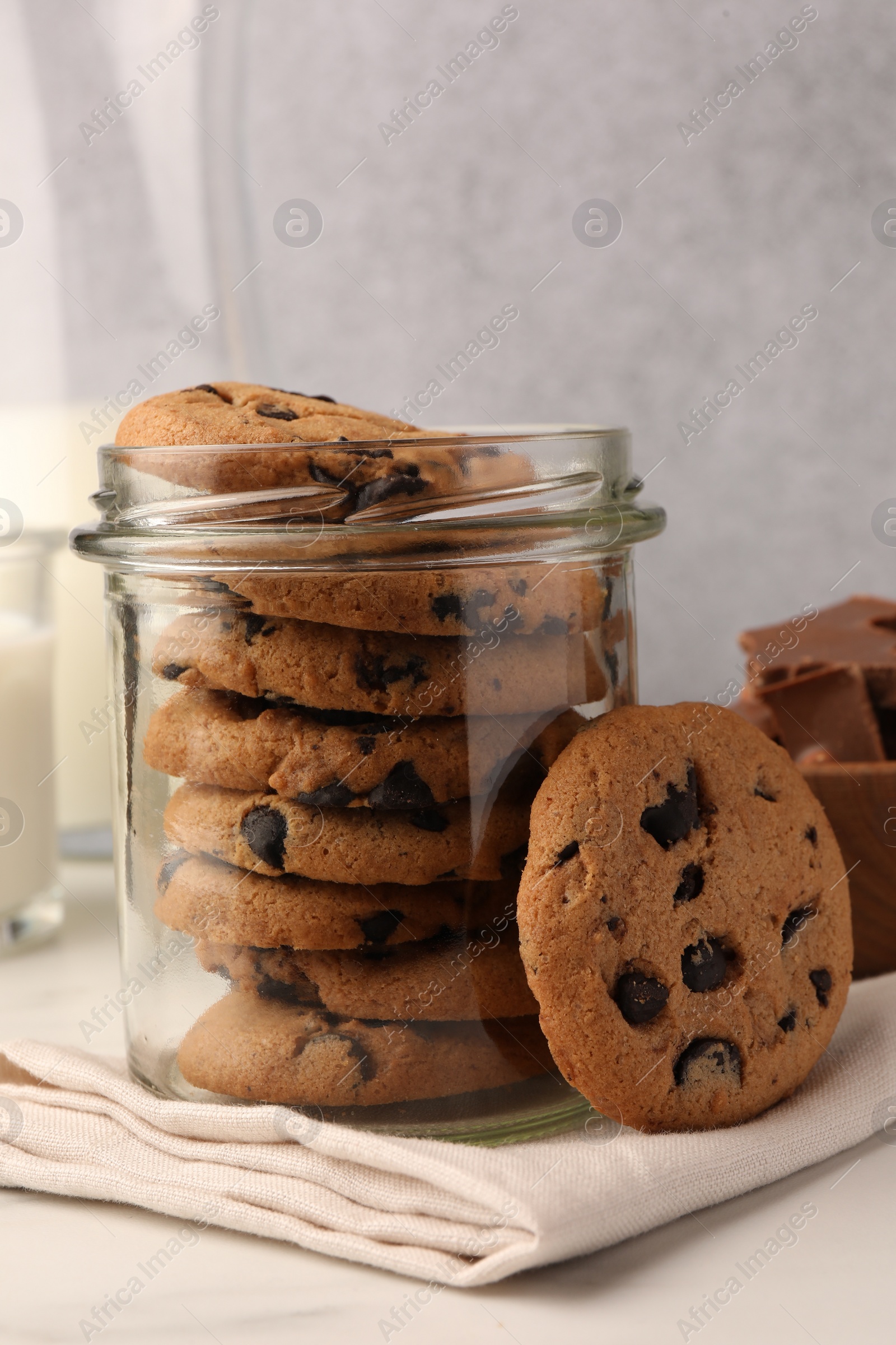 Photo of Glass jar with delicious chocolate chip cookies and milk on white marble table