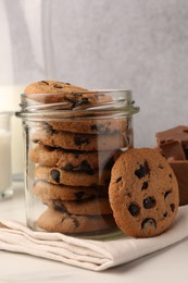 Photo of Glass jar with delicious chocolate chip cookies and milk on white marble table