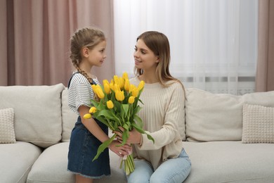 Photo of Little daughter congratulating mom with bouquet of yellow tulips at home. Happy Mother's Day