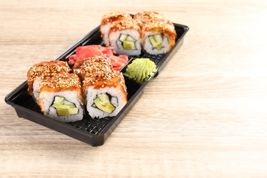 Box with tasty sushi rolls on wooden table, space for text. Food delivery