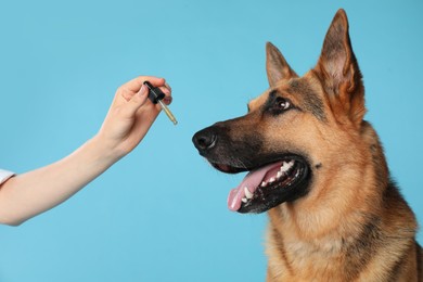 Photo of Woman giving tincture to German Shepherd dog on turquoise background, closeup