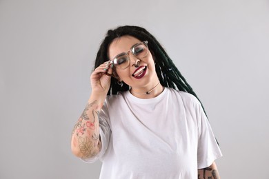 Beautiful young woman with tattoos on arms, nose piercing and dreadlocks against grey background