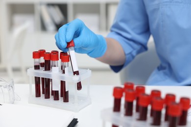 Photo of Laboratory testing. Doctor with blood samples in tubes at white table indoors, closeup