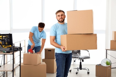 Photo of Young worker with cardboard boxes and his colleague in office. Moving service