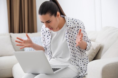 Emotional young woman with laptop at home. Online hate concept