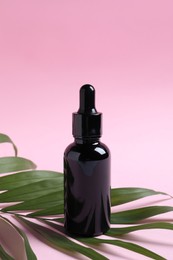 Bottle with cosmetic oil and green leaf on pink background