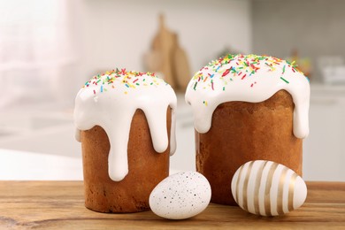 Delicious Easter cakes with sprinkles and decorated eggs on wooden board in kitchen