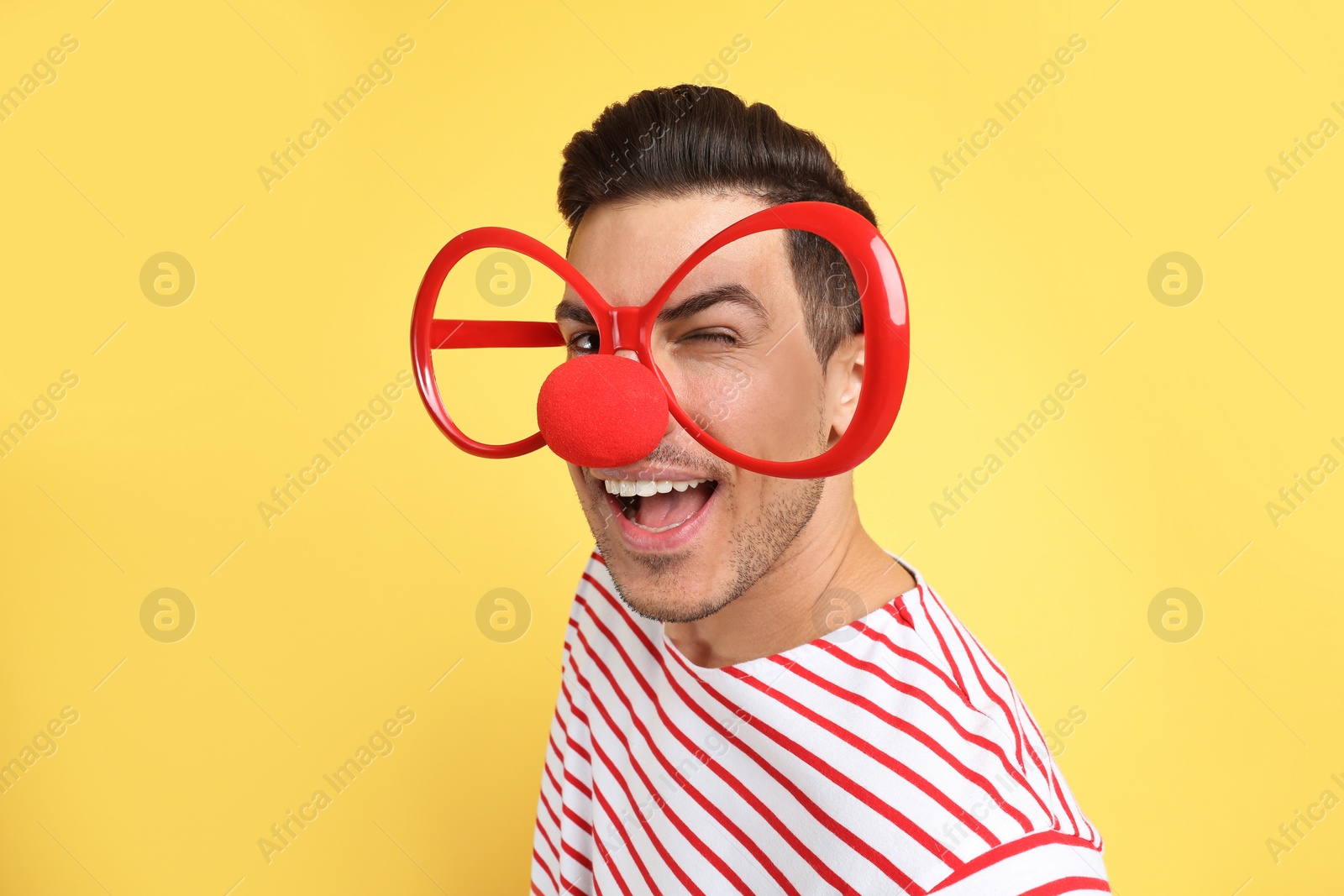 Photo of Funny man with clown nose and large glasses on yellow background. April fool's day