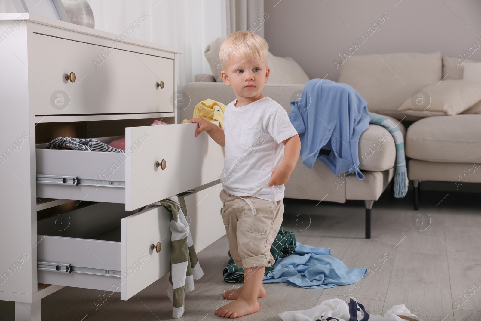 Photo of Cute little boy playing with clothes in dresser's drawer at home