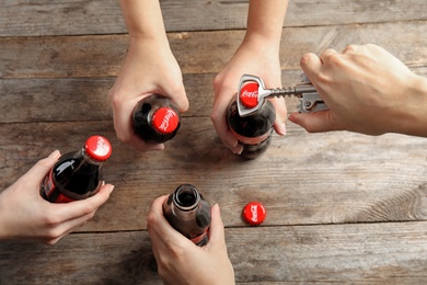 MYKOLAIV, UKRAINE - NOVEMBER 15, 2018: People with bottles of Coca Cola at wooden table, top view