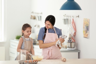 Photo of Mother and her daughter making dough at table in kitchen