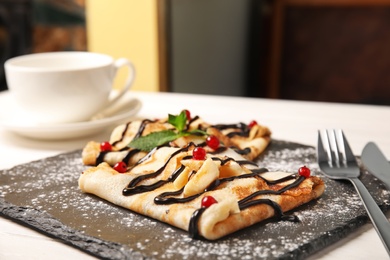 Photo of Thin pancakes served with sauce and berries on slate plate, closeup