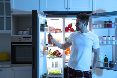 Young man taking juice out of refrigerator at night