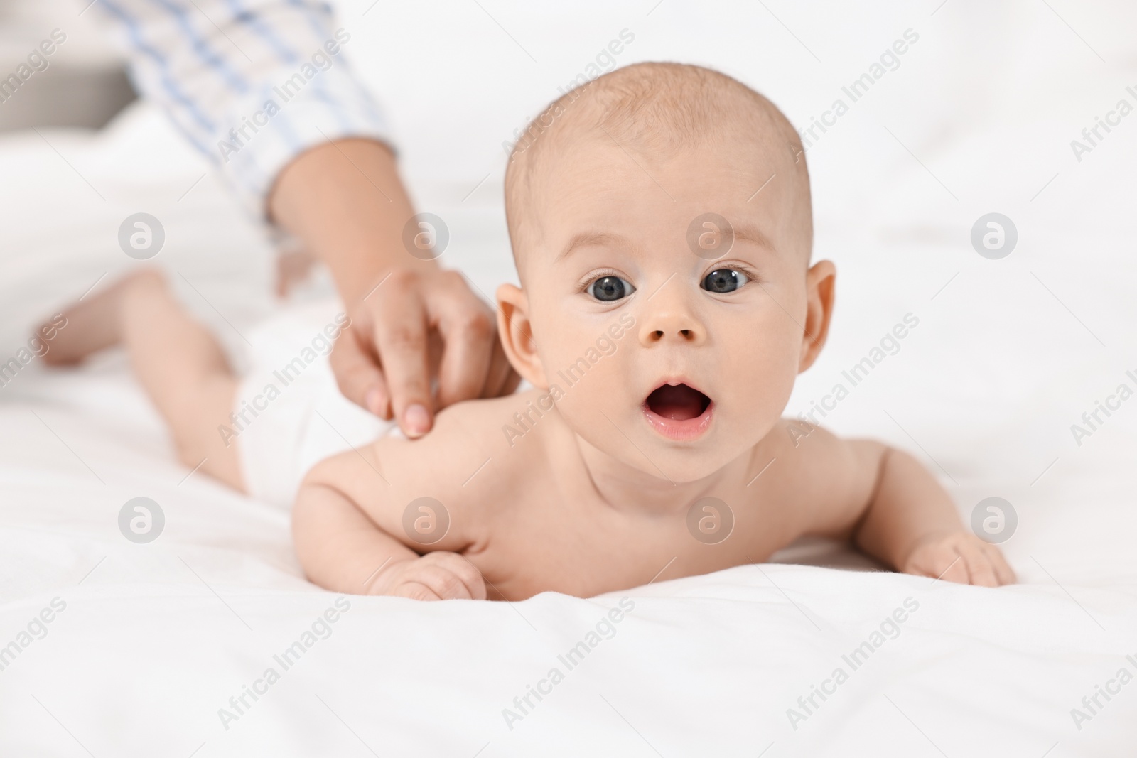 Photo of Woman applying body cream onto baby`s skin on bed, closeup