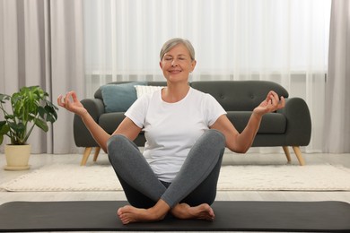 Photo of Happy senior woman practicing yoga on mat at home