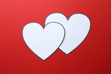 Paper hearts on red background, top view