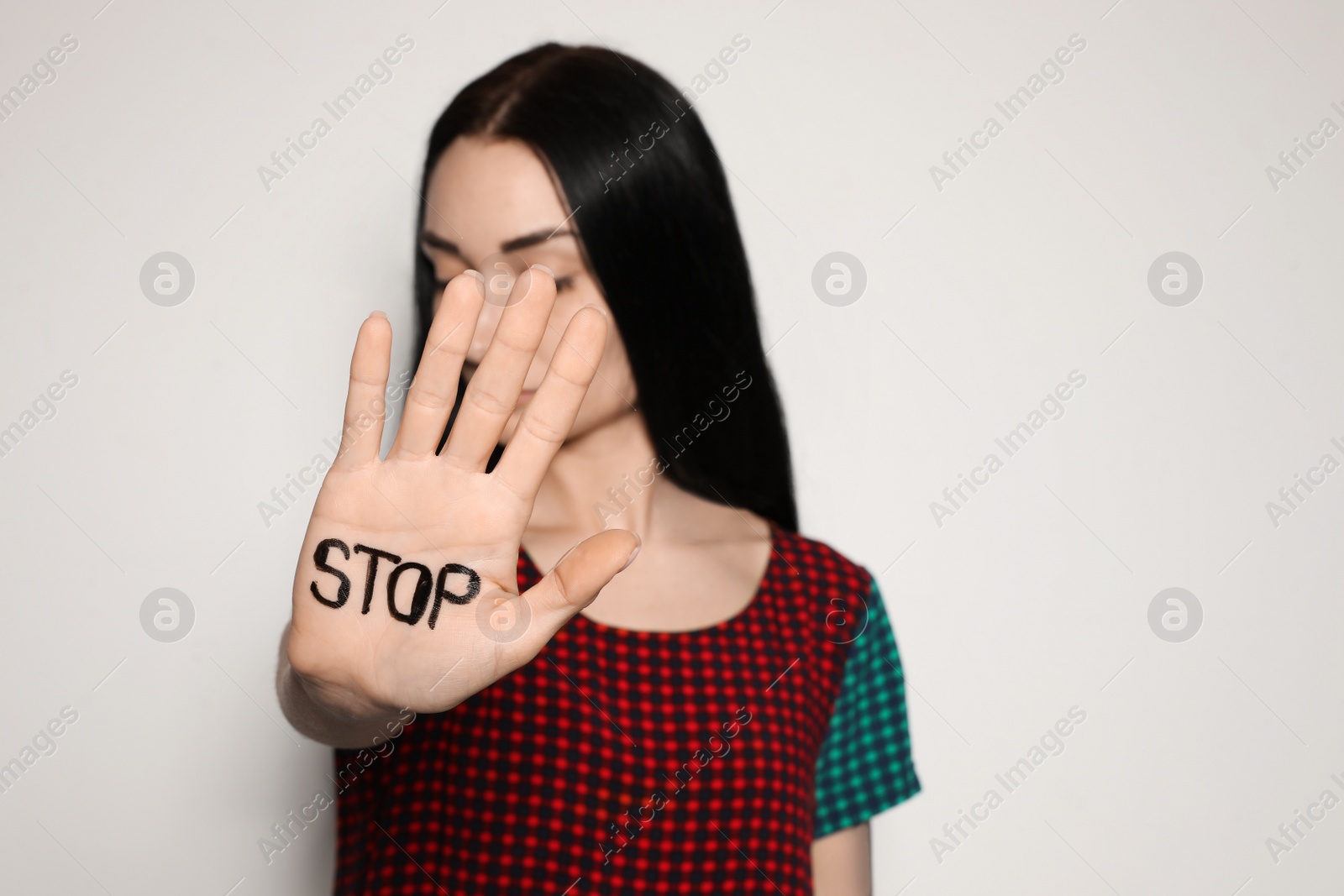 Photo of Young woman with word STOP written on her palm against light background, focus on hand. Space for text