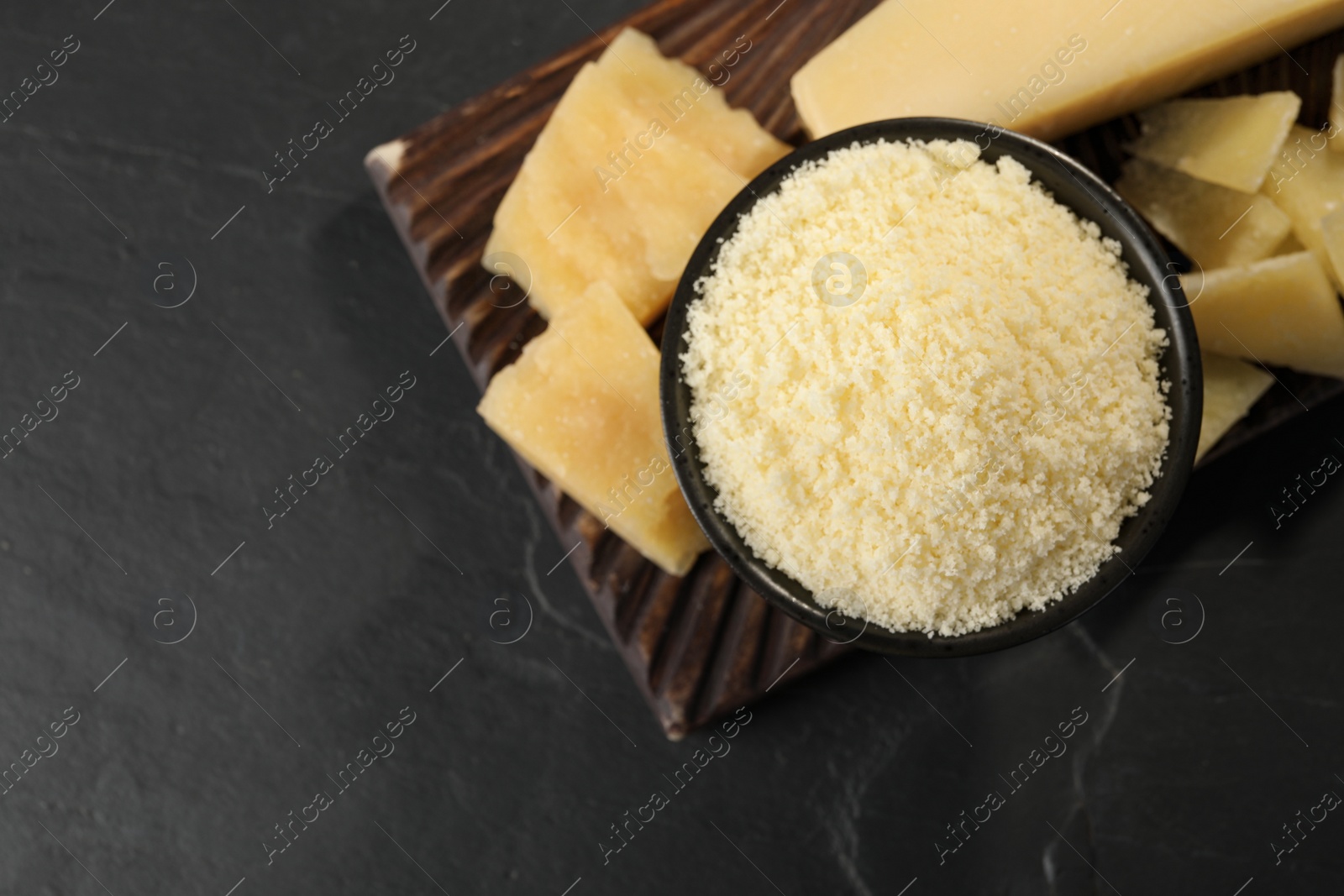 Photo of Bowl with parmesan cheese on black table, top view. Space for text