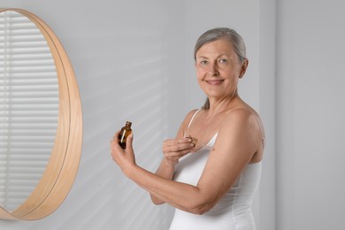 Happy woman applying body oil onto arm in bathroom