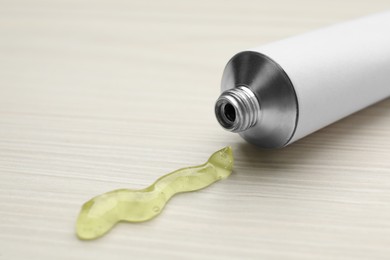 Photo of Open white tube with ointment on light wooden table, closeup