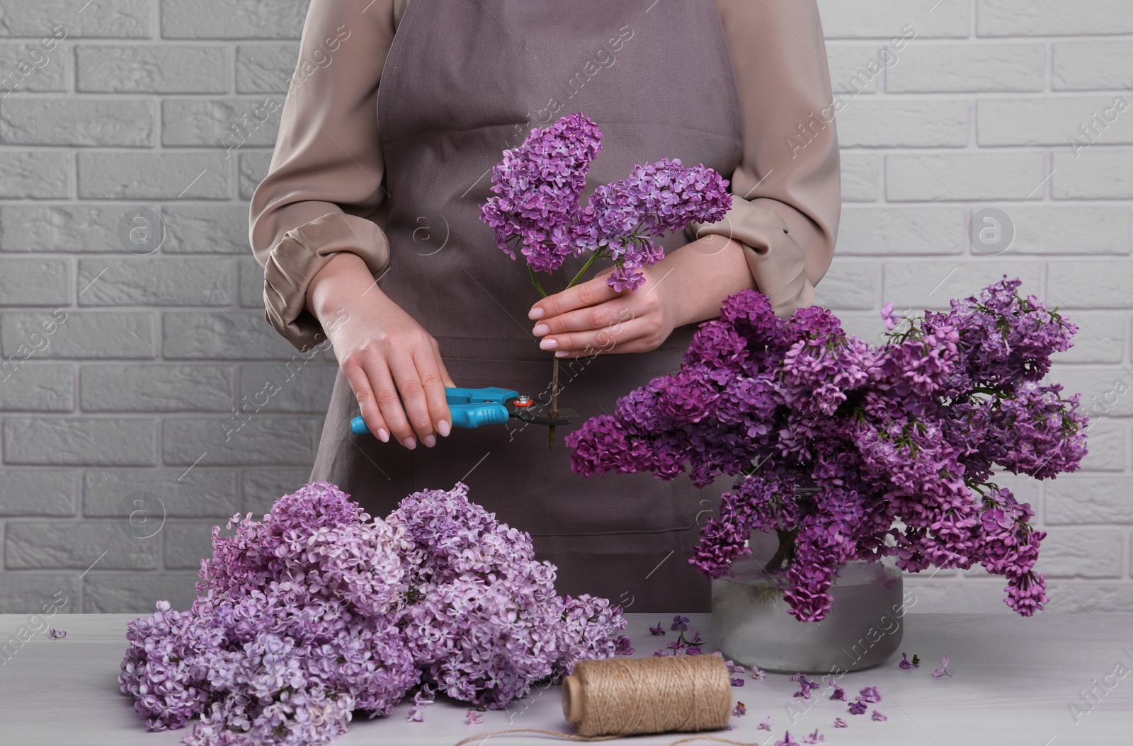 Photo of Woman trimming lilac branches with secateurs at white wooden table, closeup