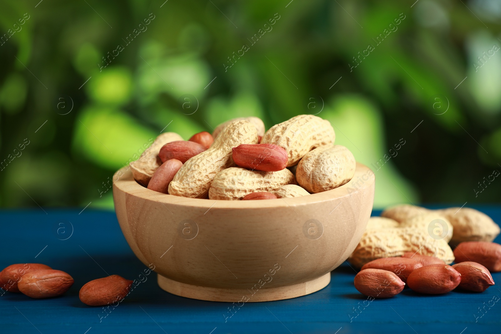 Photo of Fresh unpeeled peanuts in bowl on blue wooden table against blurred background