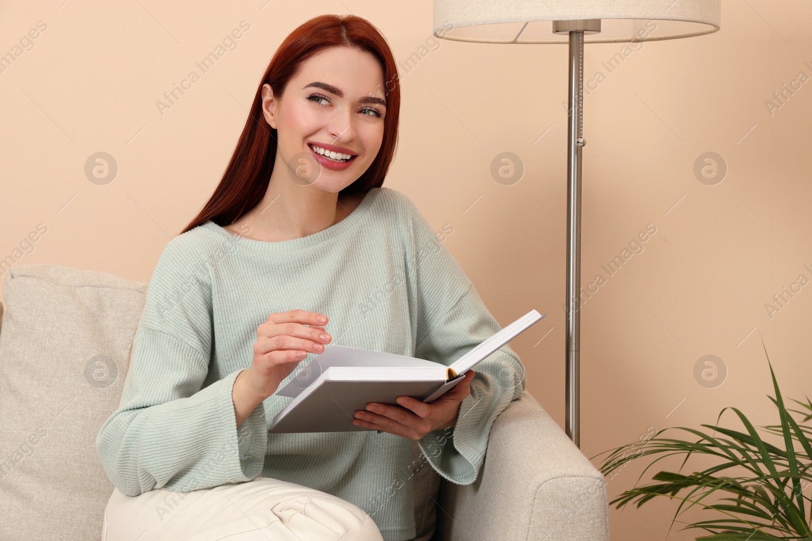 Photo of Happy woman with red dyed hair and book sitting on sofa indoors