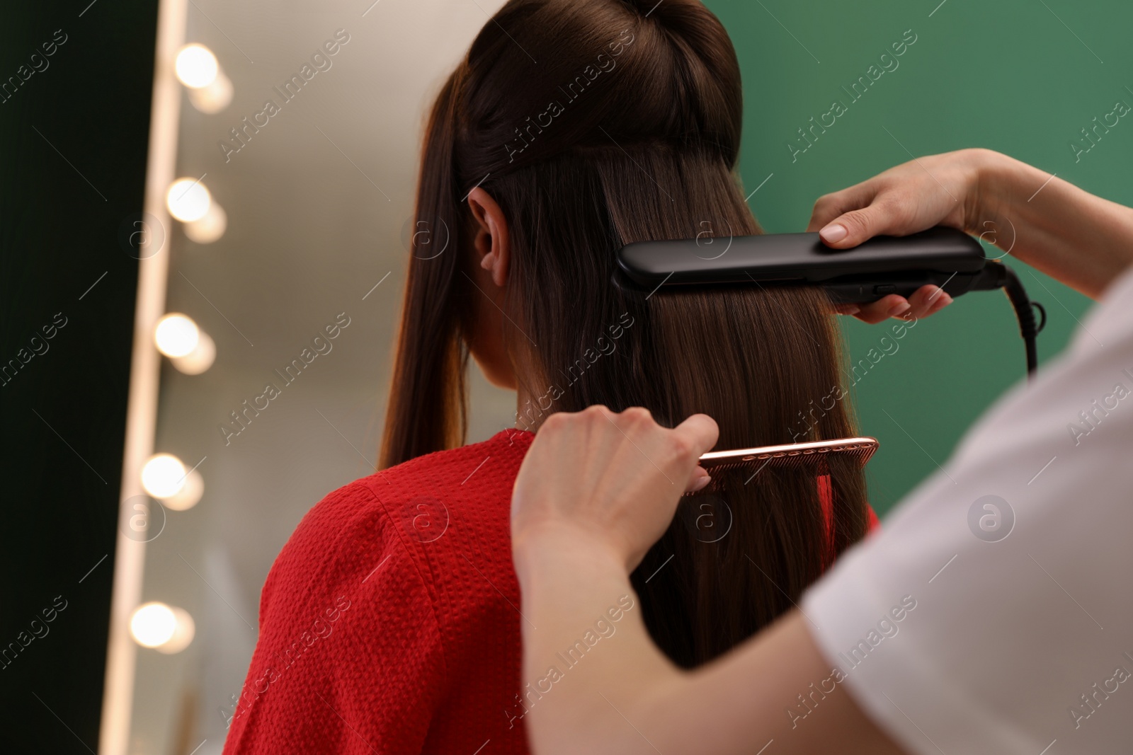 Photo of Stylist straightening woman's hair with flat iron in salon