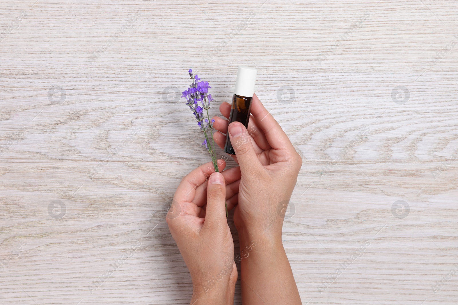 Photo of Woman with bottle of lavender essential oil and flowers on wooden background, top view