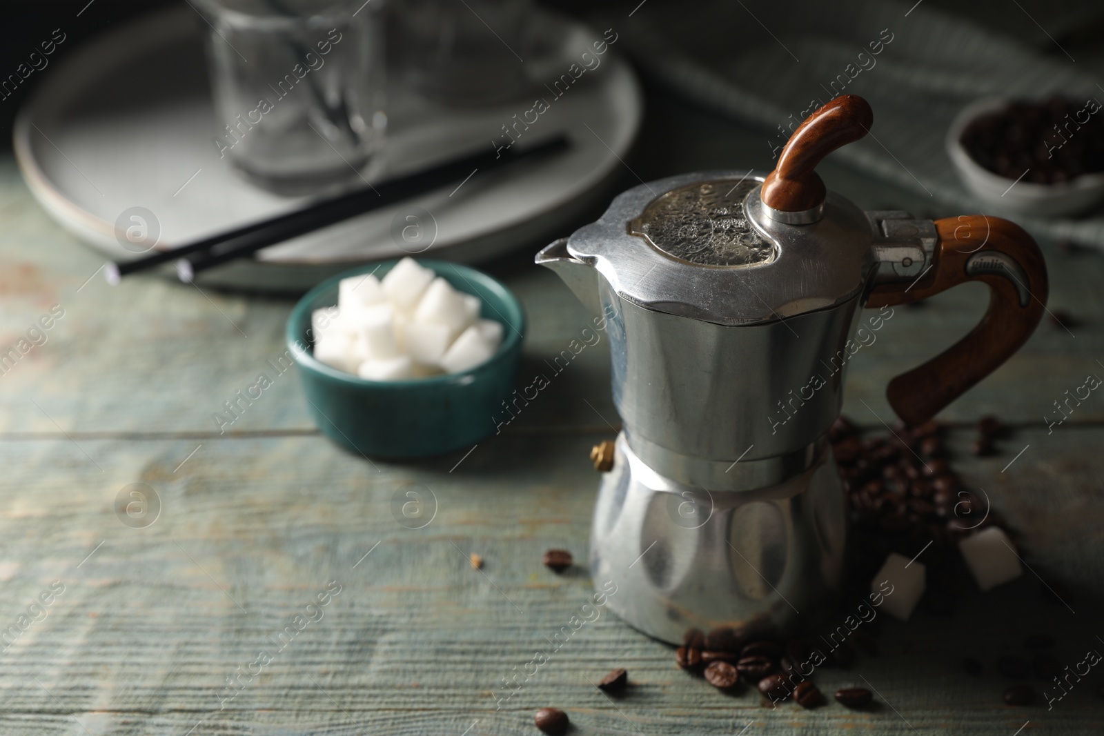 Photo of Moka pot, coffee beans and sugar cubes on rustic wooden table, space for text