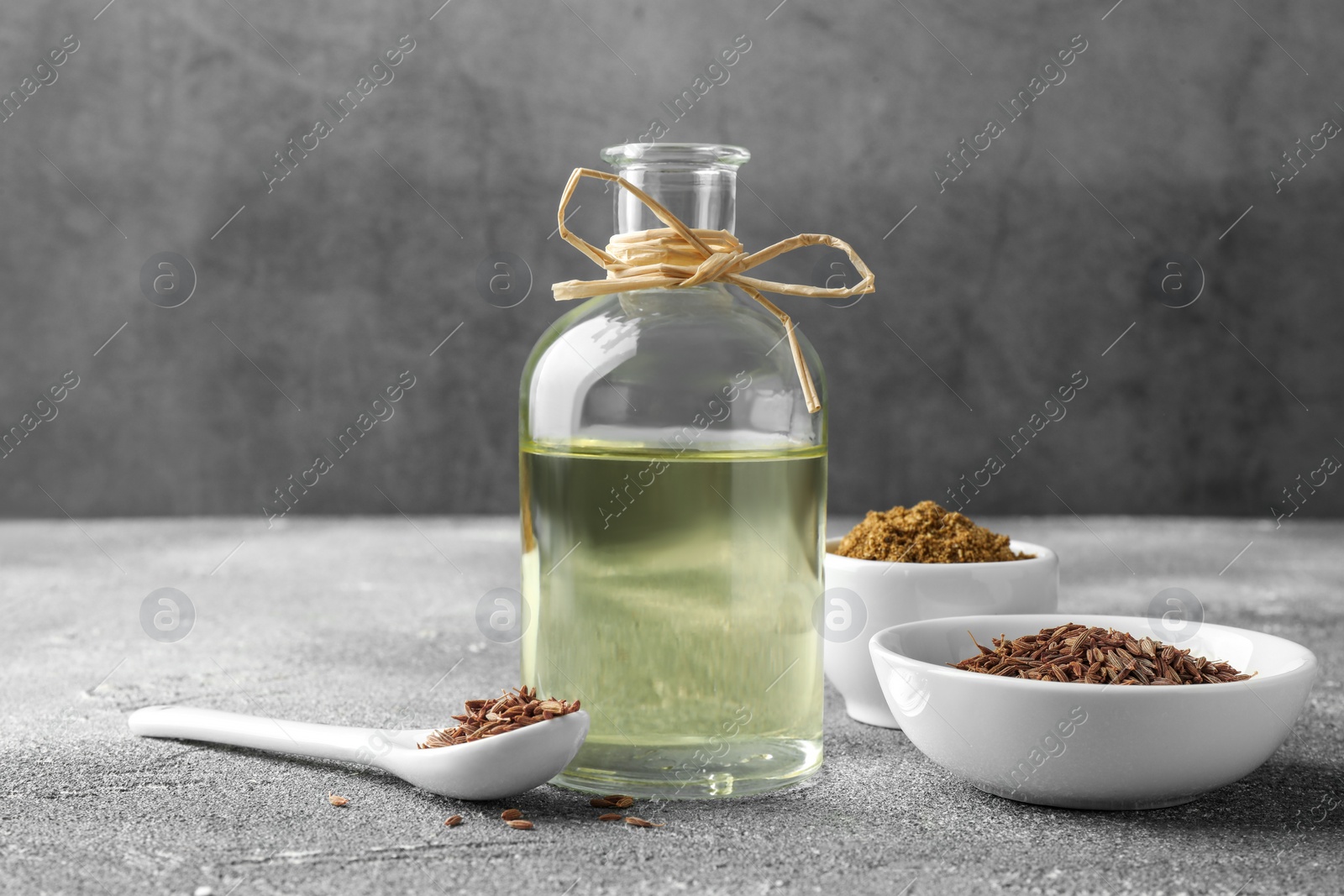 Photo of Caraway (Persian cumin) seeds, powder and essential oil on gray textured table